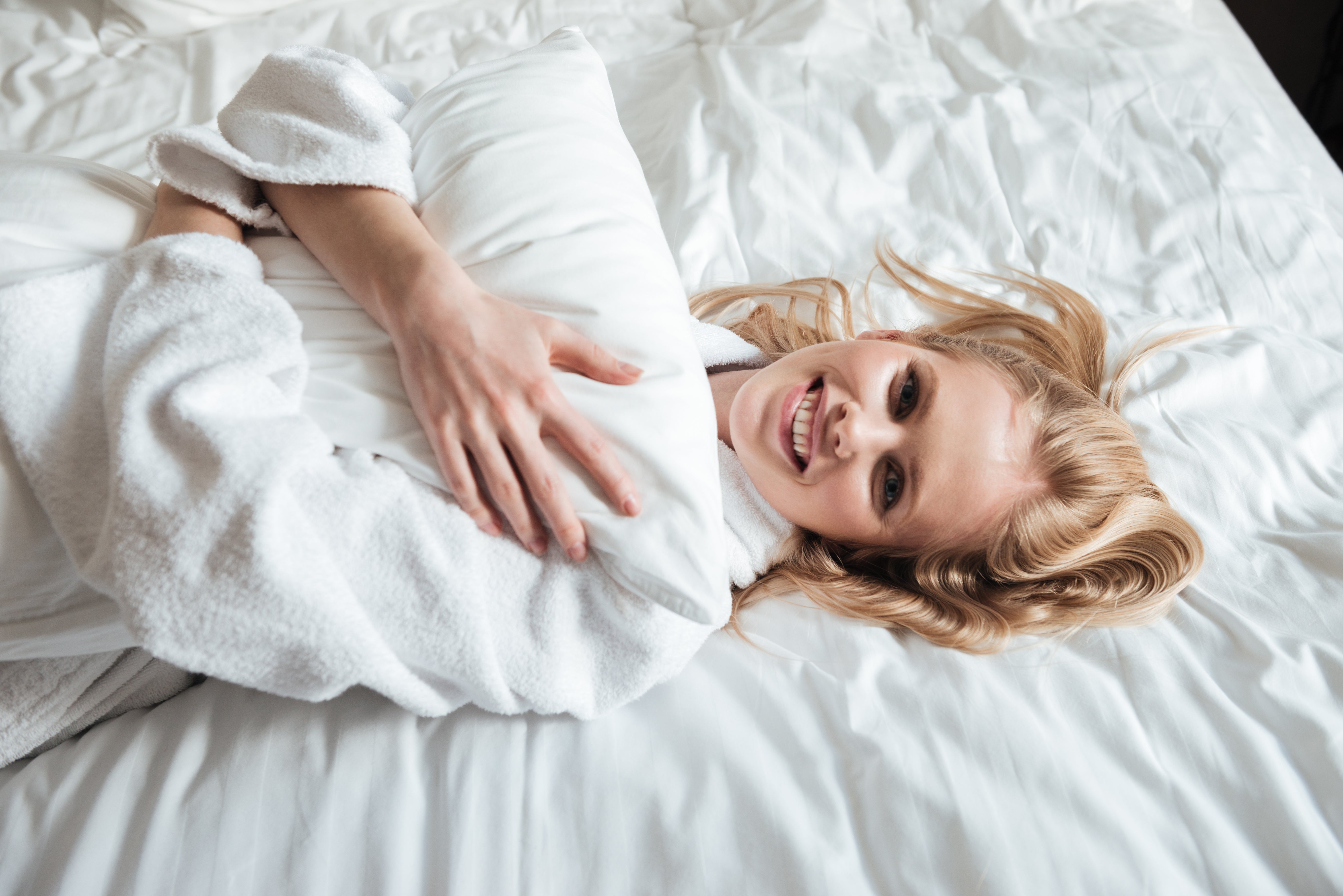 Happy young woman wearing a bathrobe, lying on her bed with a bright smile, feeling comfortable and relaxed.